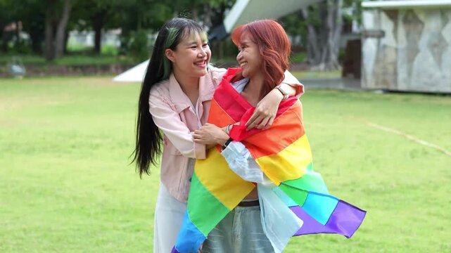 Happy Asian lesbian couple embracing with rainbow pride flag, celebrating love, equality, freedom, LGBTQ relationships, diversity and authentic lifestyle.