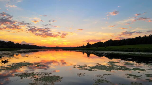 Beautiful sunset over a calm river with vibrant orange and blue sky reflecting on the water surface in a peaceful nature landscape