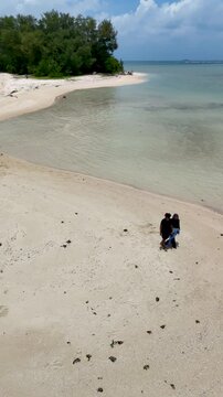 A couple walks along the white sandy beach at Kerayaan Beccu Beach and smiles at the camera