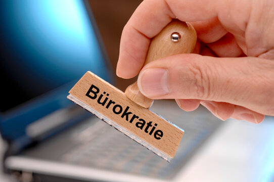Eine Hand h&auml;lt einen Holzstempel mit der Aufschrift: B&uuml;rokratie