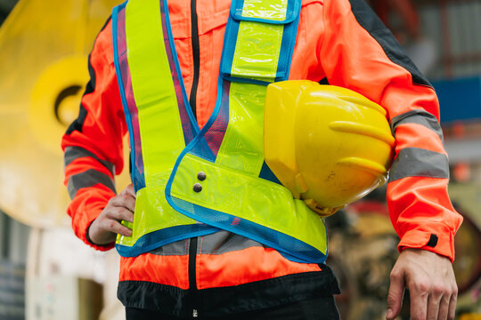 Industrial concept. Construction worker in reflective vest holding hard hat at industrial site with safety gear and focused pose