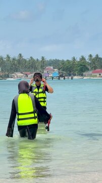 A young couple on the beach is preparing to go swimming with snorkeling gear on a sunny day