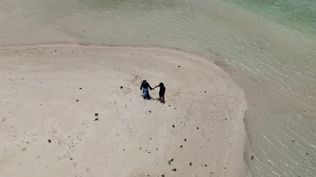 A couple walks along the white sandy beach at Kerayaan Beccu Beach and smiles at the camera