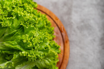 Fresh green leafy lettuce on wooden plate. Crisp, vibrant greens with ruffled edges. Natural lighting highlights texture and freshness © sidoel98