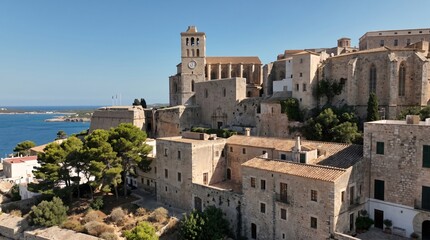 Fototapeta premium A view of the historic Ibiza Cathedral and Dalt Vila old town with traditional stone architecture overlooking the Mediterranean Sea under a clear blue sky.