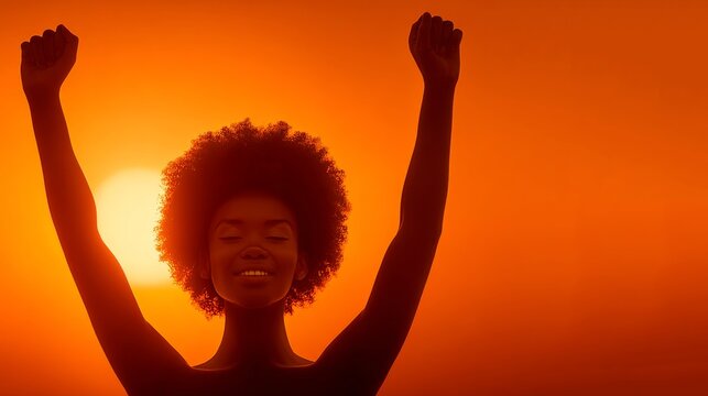 A silhouette photograph of a smiling Black woman with an afro hairstyle raising her arms in victory against a vibrant orange sunset background.