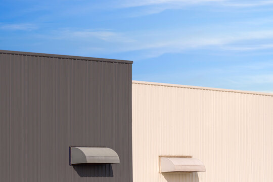 Industrial factory building facade with dryer vent on gray and white corrugated metal wall in modern minimal style against blue sky background.