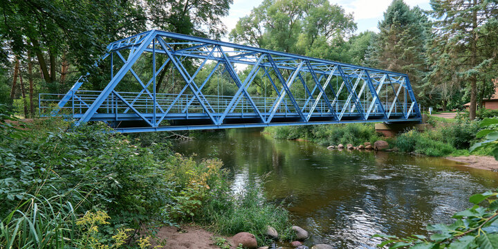 Blue metal truss bridge spanning a scenic river surrounded by greenery