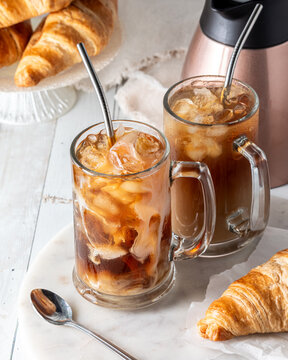 Two glasses of freshly poured iced coffee against a light background.