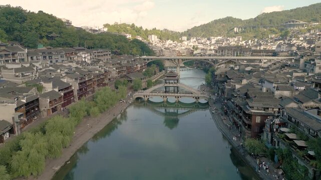 Horizontal 4K UHD aerial drone shot flying forward and tilting down over Xueqiao Bridge and Tuojiang River with traditional architecture in historic Fenghuang Ancient Town Hunan China
