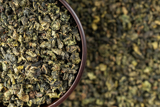 Wooden cup full of green oolong surrounded by loose tea texture