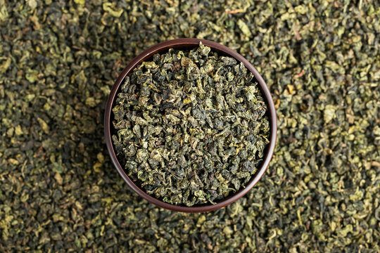 Wooden cup full of green oolong surrounded by loose tea texture
