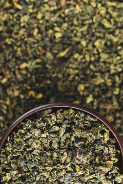 Dark wood bowl overflowing with Tie Guan Yin on full tea background