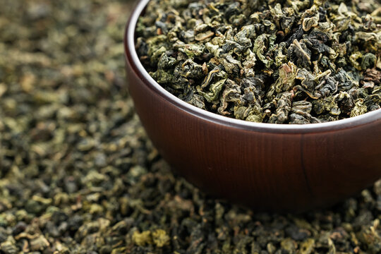 Wooden cup full of green oolong surrounded by loose tea texture
