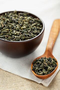 Overhead macro wooden cup and spoon filled with Tieguanyin on burlap fabric