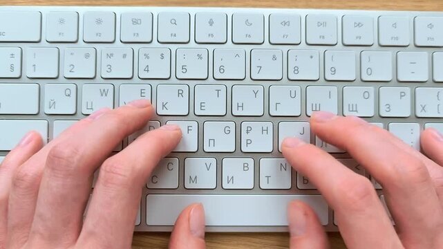 Close-up of hands typing on a computer keyboard. Top-down view showing fingers pressing keys at a desk. Detailed office scene of everyday digital work..
