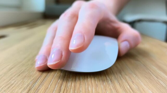 Close-up of female fingers clicking a computer mouse. Woman's hand navigating during everyday digital work. Detailed scene of office equipment in use..