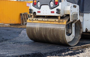 Construction worker uses a road roller to flatten asphalt on a new road at a construction site...