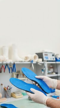 Blue custom orthotic insoles held in laboratory by gloved hands for foot health awareness product display and medical device banner