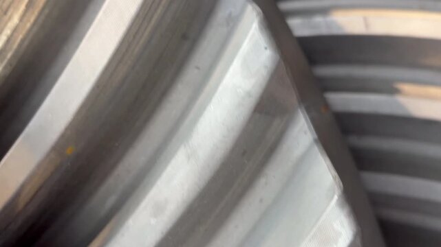 Tight oblique close-up shows heavy machined metal gears with broad concentric ridges, shallow grooves, fine horizontal texture, scattered dust, scratches, and muted gray tonal contrast 4K footage