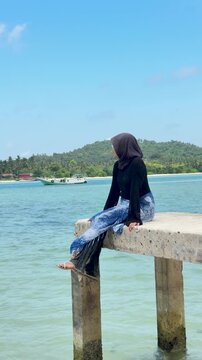 A young woman sits on a beach pier in Kotabaru, gazing out at the sea