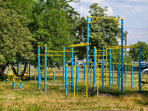 Yellow and blue outdoor fitness area with gymnastic rings pull up bars parallel bars and stationary training equipment in a residential neighborhood for exercise and recreation