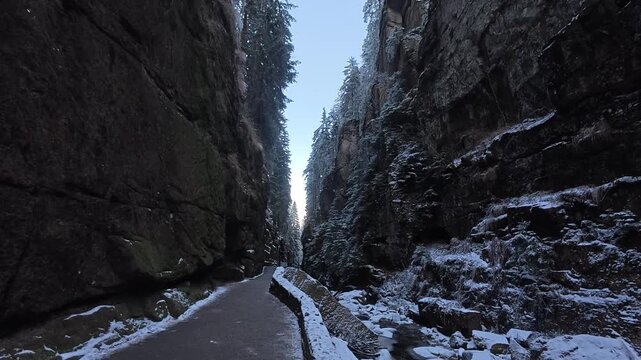 A narrow gorge runs between tall rocky cliffs in a dramatic natural landscape. The video captures rugged terrain, shadowed rock walls, and outdoor mountain scenery.