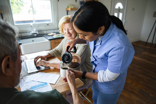 Caregiver pouring coffee for senior couple at home kitchen