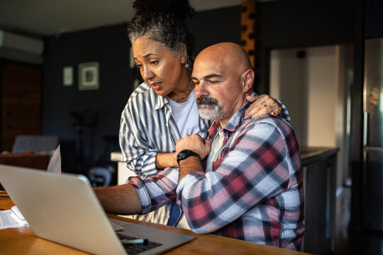 Concerned mature couple reviewing finances at home on laptop