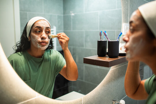 Woman applying face mask with brush in bathroom mirror