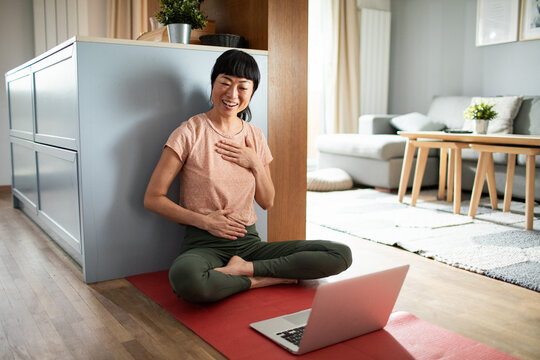 Smiling woman practicing online breathwork meditation at home