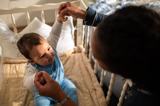 Parent helping baby sit up in crib at home