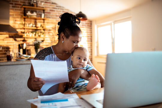 Mother paying bills online while holding baby at home