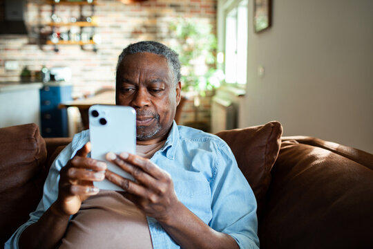 Senior man using smartphone on sofa at home