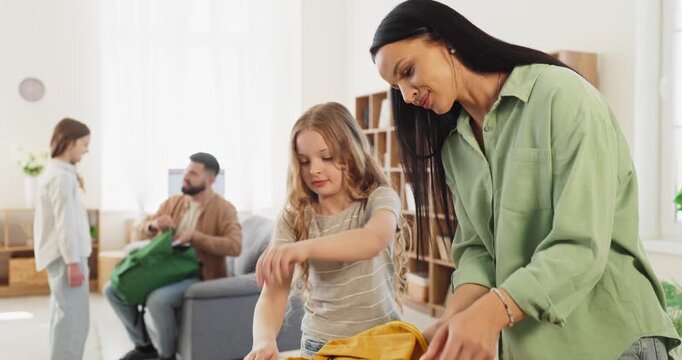 Family parents help children with school backpacks. Morning routine at home as parents help two girls pack supplies in preparation before class. Clear back to school family concept.