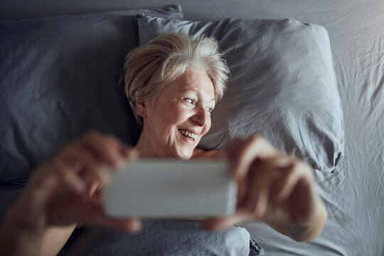 Senior woman taking smartphone selfie in bed