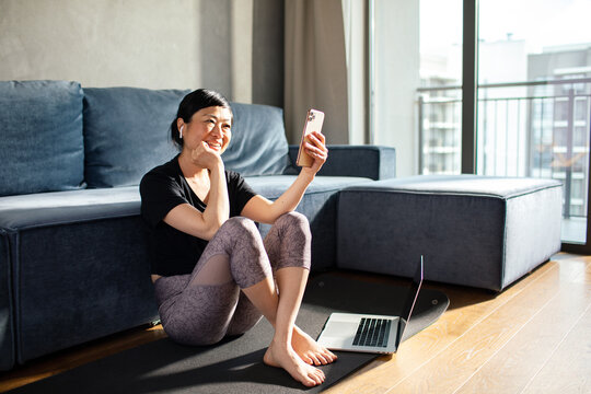 Smiling woman video chatting on smartphone after home workout in living room