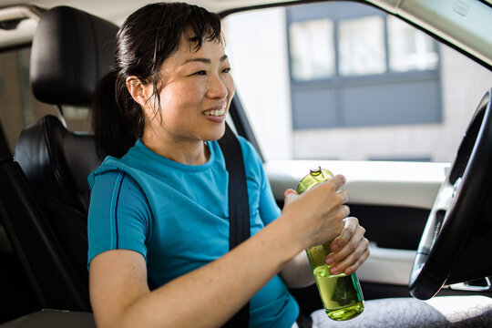 Smiling woman driver drinking water in car