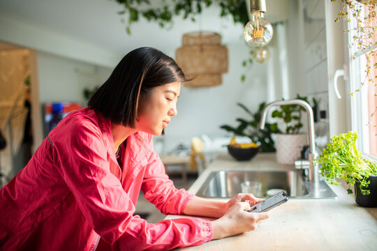 Woman using smartphone in bright modern home kitchen