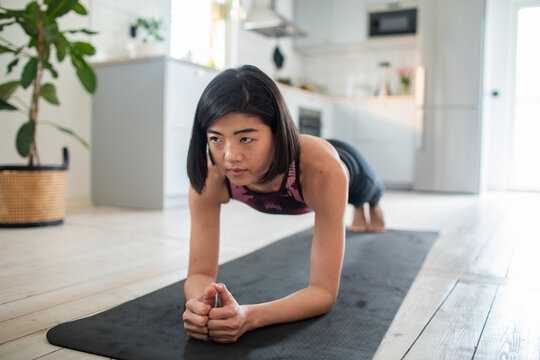 Focused young woman doing plank exercise at home in kitchen