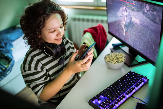 Teen gamer using smartphone at home pc setup