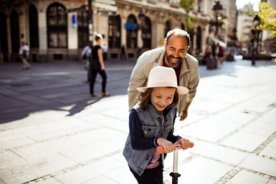 Parent and child riding scooter on sunny city street