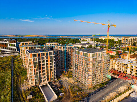 Construction site of new buildings near the coast with cranes, machinery, and workers visible under a clear blue sky