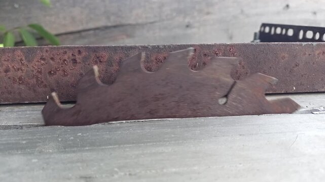 Close up of old rusty circular saw blade slowly rotating on workbench slot in carpentry workshop
