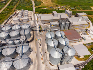 Industrial site with grain silos and processing buildings near a road in a rural area during bright daylight © DSMT
