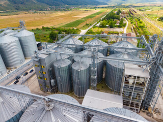 View of large grain silos and farming fields under bright sunlight in a rural area during daytime © DSMT