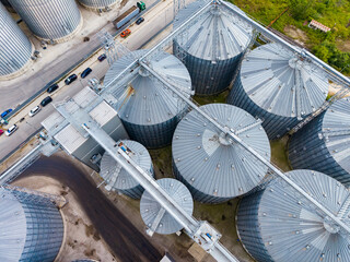 Grain storage facility with metal silos and trucks on the road near a green area during daylight © DSMT