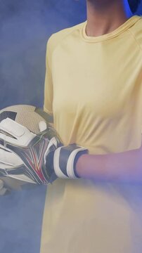 Vertical video: Camera panning, keeper holding ball turning in studio shoot with gloves, yellow top