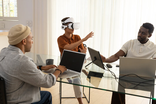 Diverse male team testing VR demo at meeting room glass table with headset, controller, laptops