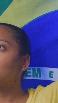 Vertical video: Opening camera on woman in yellow shirt raising arm with Brazil flag, copy space